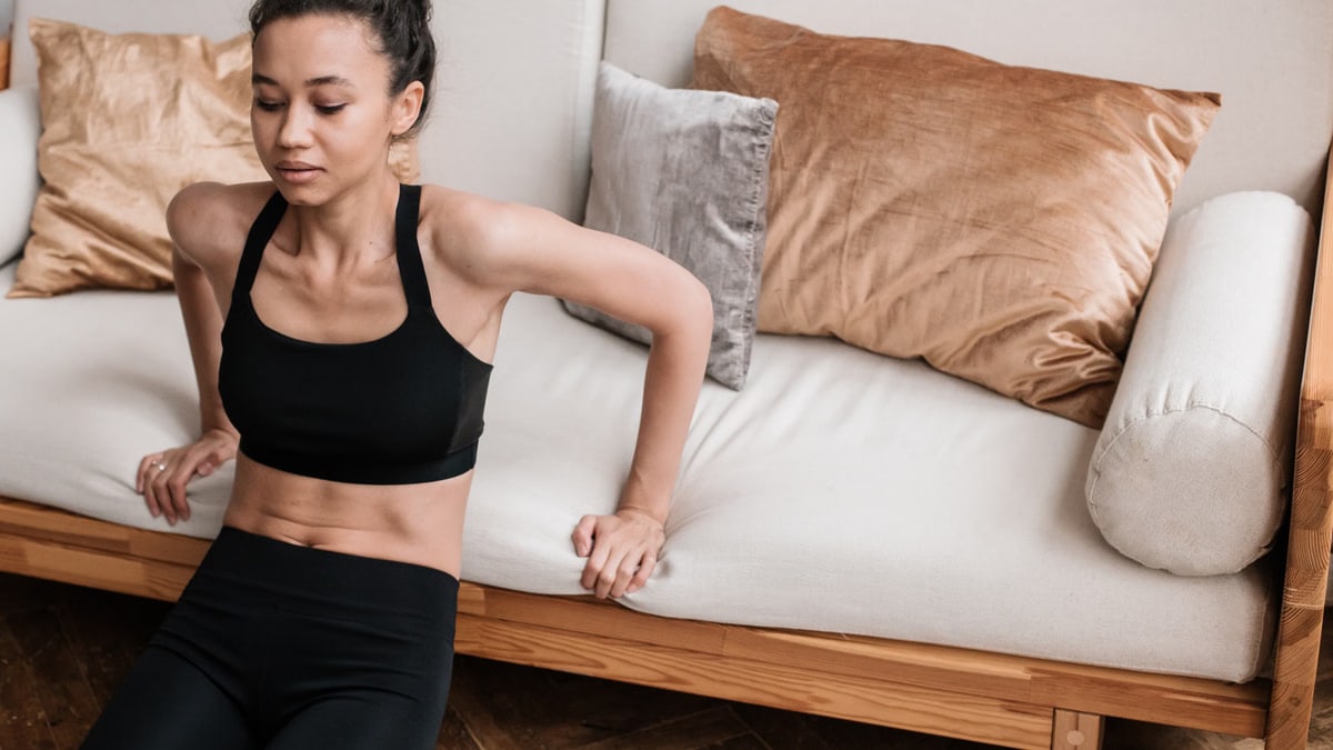 Adult woman in sportswear doing a workout at home on a couch. Focus on fitness and healthy lifestyle.