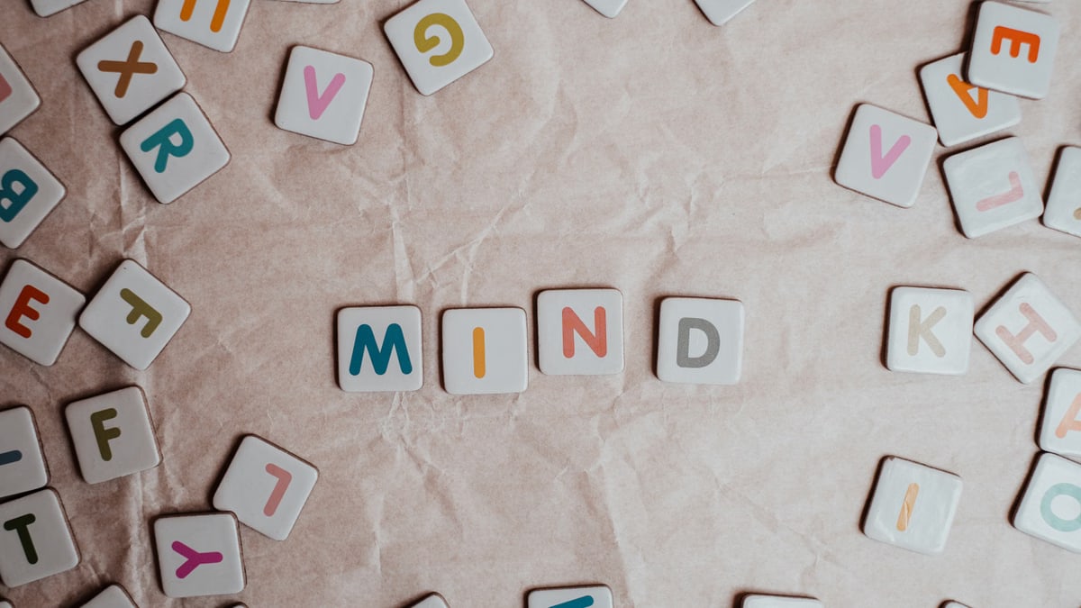 Close-up of scattered letter tiles spelling 'mind' on crumbled paper background.